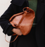 Person holding a brown leather bag with text about modern heritage and craftsmanship.